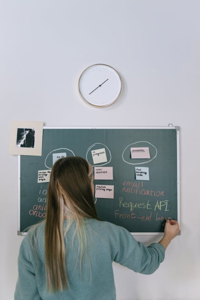 A young woman writes on a blackboard in a contemporary office setting, engaging in creative project planning.